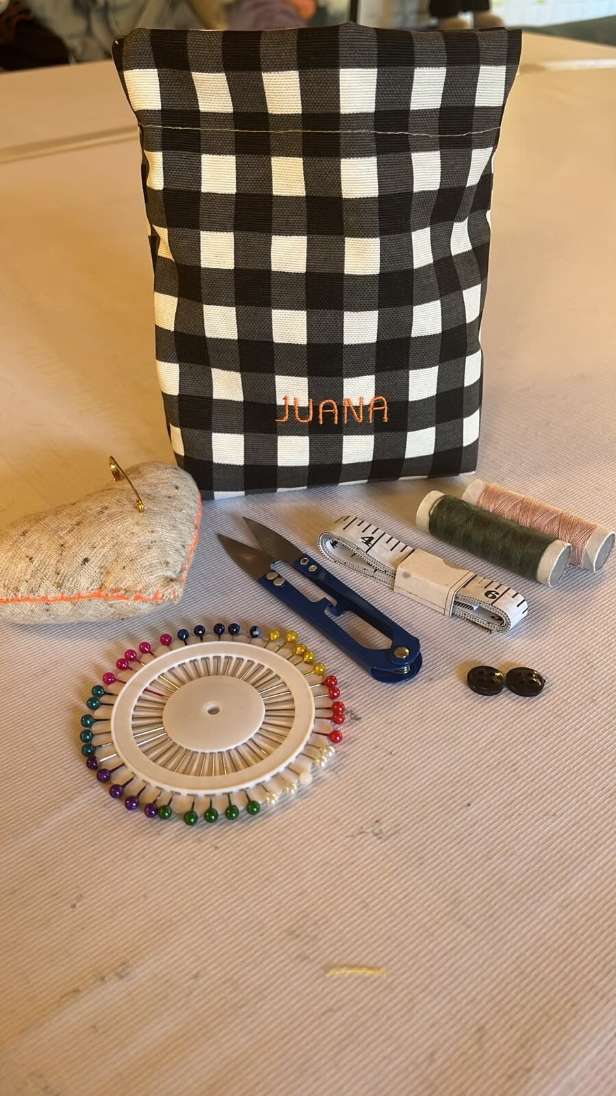 Una bolsa terminada con el nombre Juana, junto a tijeras, carretes, alfileres y huincha de medir