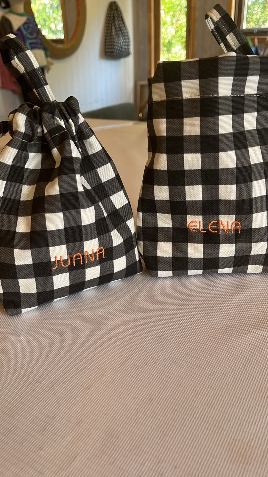 Dos bolsas de cuadrillé blanco y negro con los nombres Juana y Elena bordados en hilo naranja