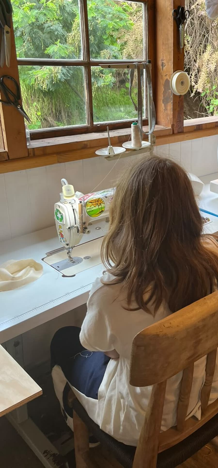 Una niña, de espaldas, cose en una máquina frente a la ventana del taller